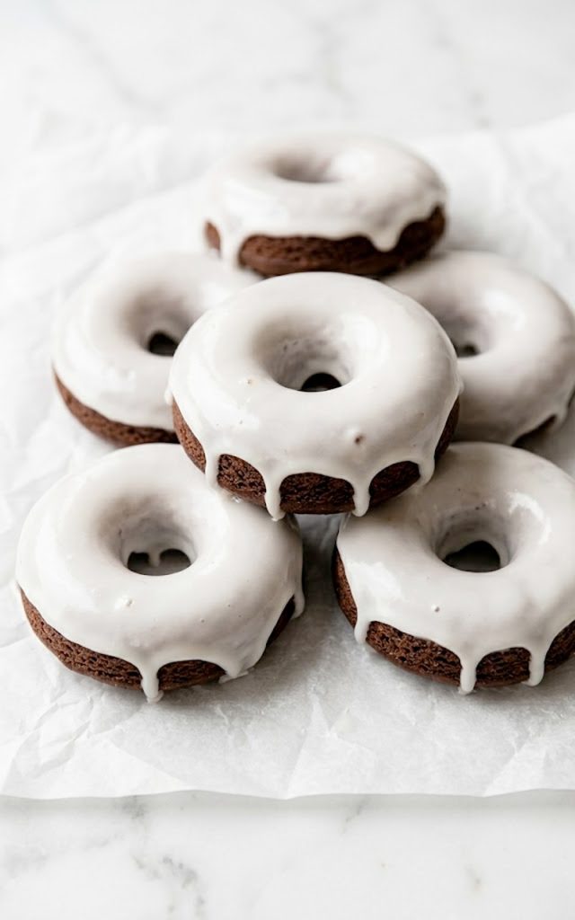 Easy chocolate cake donuts with vanilla glaze stacked on parchment paper with glaze dripping down the sides