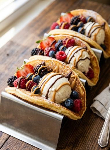 Overhead view of three golden pancake tacos in a metal taco rack filled with vanilla ice cream, fresh berries, chocolate drizzle, and peanut butter