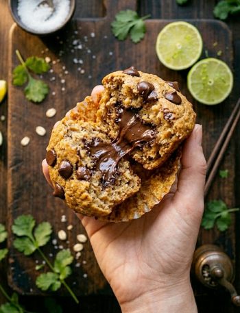 Soft flourless peanut butter banana muffins with melty chocolate chips on a white plate, one muffin broken open to reveal the fudgy chocolate center
