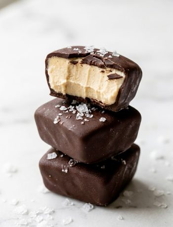 A stack of frozen peanut butter Greek yogurt bites coated in dark chocolate with flaky sea salt on top one bitten open to reveal the creamy peanut butter center