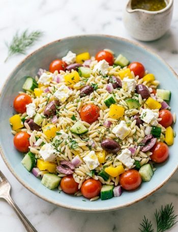 Overhead shot of Greek orzo pasta salad in a light blue bowl with cherry tomatoes, cucumber, feta, kalamata olives, and fresh herbs