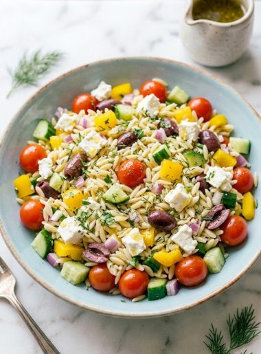 Overhead shot of Greek orzo pasta salad in a light blue bowl with cherry tomatoes, cucumber, feta, kalamata olives, and fresh herbs