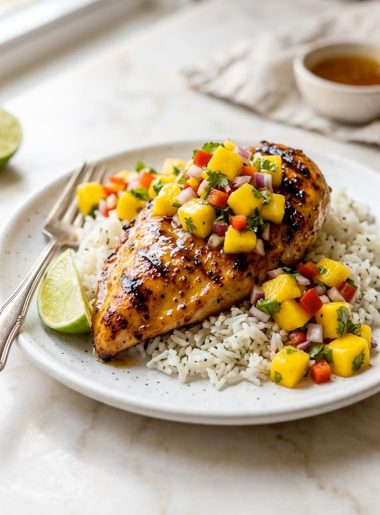 A white plate with honey lime grilled chicken breast showing beautiful grill marks, topped with vibrant fresh mango salsa and served over fluffy white rice with a lime wedge
