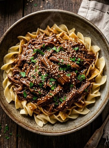 A bowl of slow cooker Korean beef noodles topped with sesame seeds and fresh parsley on a rustic wooden table