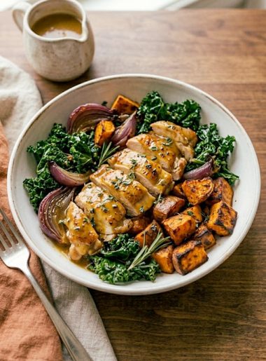 A stunning bowl of maple Dijon chicken with caramelized roasted sweet potatoes wilted kale and roasted red onion drizzled with a golden maple Dijon sauce in a wide ceramic bowl