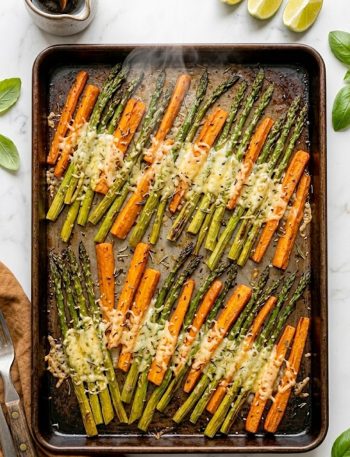 A sheet pan of oven-roasted asparagus spears and carrot sticks caramelized and golden with melted parmesan cheese and fresh herbs on top