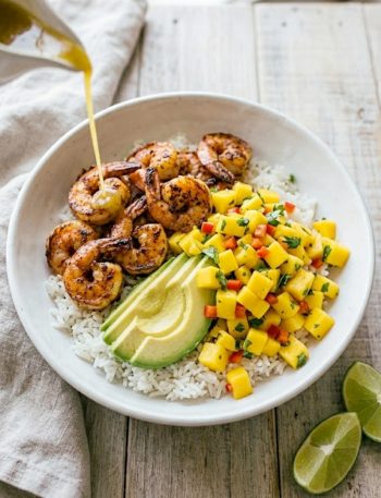 A vibrant shrimp and avocado bowl with mango salsa and lime-chili sauce drizzled on top, served over white rice