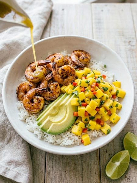 A vibrant shrimp and avocado bowl with mango salsa and lime-chili sauce drizzled on top, served over white rice