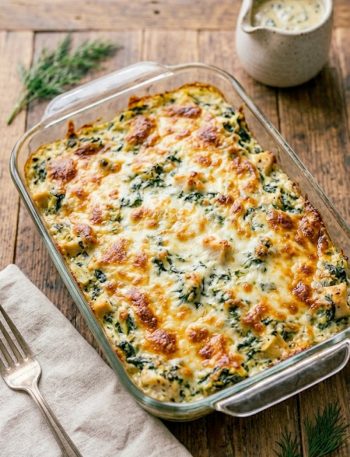 Golden bubbly spinach artichoke chicken bake fresh out of the oven in a glass baking dish with melted cheese on top