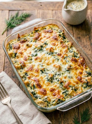 Golden bubbly spinach artichoke chicken bake fresh out of the oven in a glass baking dish with melted cheese on top