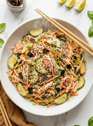 A white bowl of sushi cucumber salad with imitation crab, sliced cucumbers, nori pieces, black sesame seeds and creamy spicy mayo dressing with chopsticks resting on the side