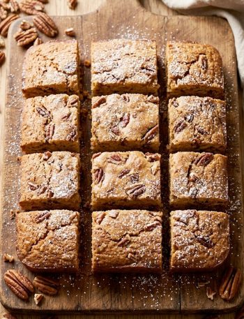 Golden brown sweet Alabama pecan bread cut into squares on a rustic wooden board with whole pecans scattered around