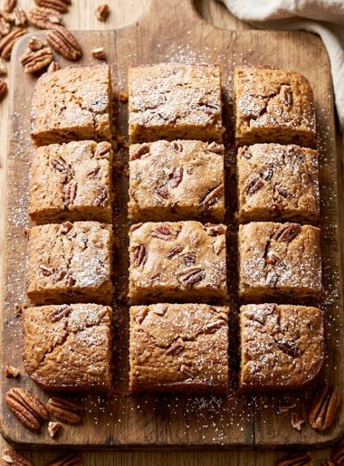 Golden brown sweet Alabama pecan bread cut into squares on a rustic wooden board with whole pecans scattered around
