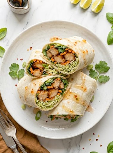 Two sweet chili chicken wraps cut in half and stacked on a white plate showing the glossy glazed chicken crunchy cabbage slaw shredded carrots fresh cilantro and lime wedges