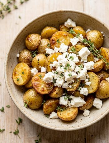 Crispy roasted baby potatoes topped with crumbled feta cheese and fresh thyme in a rustic ceramic bowl