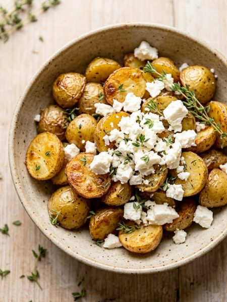 Crispy roasted baby potatoes topped with crumbled feta cheese and fresh thyme in a rustic ceramic bowl