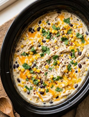 A slow cooker filled with creamy shredded fiesta chicken with black beans corn and melted cheese