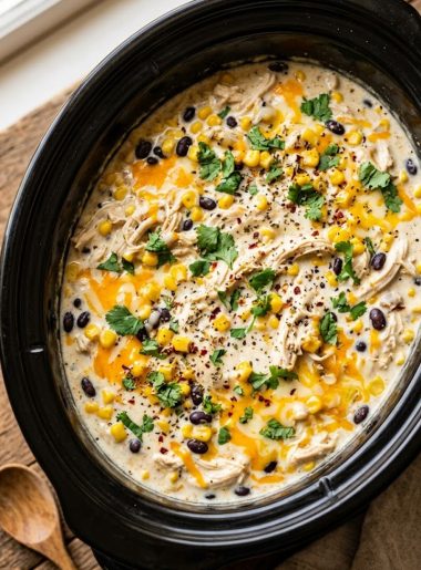 A slow cooker filled with creamy shredded fiesta chicken with black beans corn and melted cheese