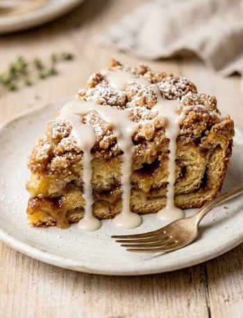 A warm slice of gooey cinnamon roll dump cake drizzled with vanilla glaze on a ceramic plate