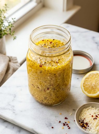 A glass jar of homemade parmesan vinaigrette with visible garlic parmesan and red pepper flakes on a marble surface