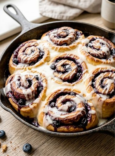 A pan of freshly baked blueberry rolls dripping with cream cheese glaze, golden brown and gooey