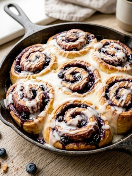 A pan of freshly baked blueberry rolls dripping with cream cheese glaze, golden brown and gooey
