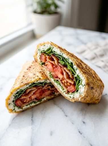 A golden baked cottage cheese wrap filled with crispy bacon slices fresh tomato and arugula folded and cut diagonally on a white marble surface showing the layers inside