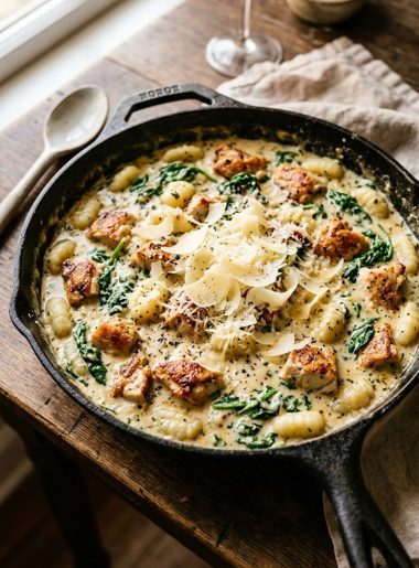 Overhead close-up of creamy chicken gnocchi in a wide skillet showing golden seared chicken pieces, pillowy gnocchi and wilted spinach in a velvety parmesan cream sauce topped with shaved parmesan