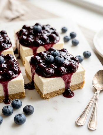 Creamy no bake keto cheesecake bars with blueberry compote topping on a white serving plate