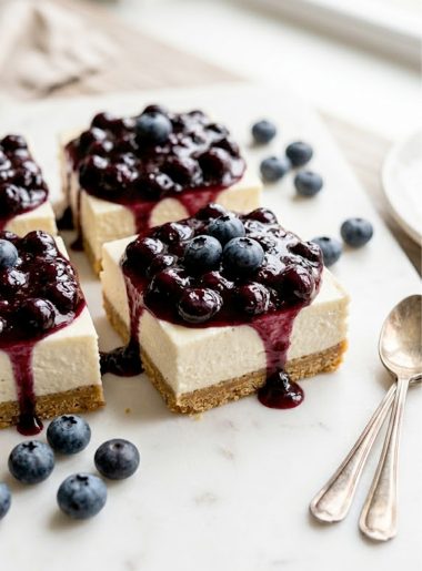 Creamy no bake keto cheesecake bars with blueberry compote topping on a white serving plate