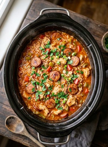 A hearty crockpot chicken jambalaya with tender chicken chunks, smoky andouille sausage slices, red and green bell peppers, and seasoned rice in a black slow cooker garnished with fresh parsley and green onions