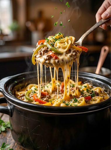 A close-up of crockpot cheesesteak tortellini being lifted with a spoon showing melted cheese, ground beef, bell peppers, and cheese-filled tortellini in a rich creamy sauce