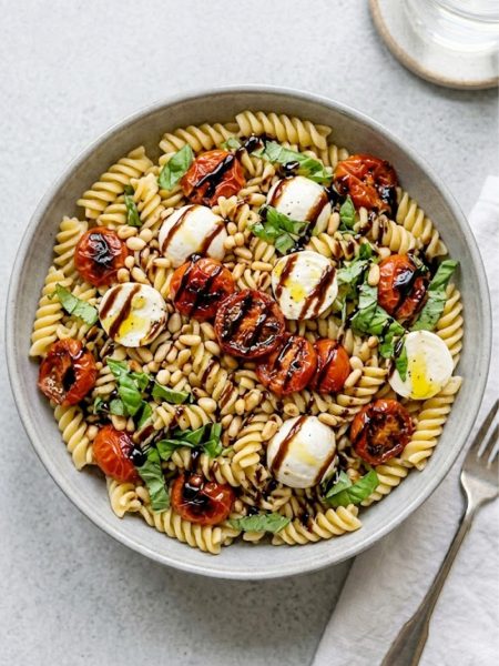 A large gray ceramic bowl filled with easy caprese pasta salad made with rotini pasta roasted cherry tomatoes fresh mozzarella balls pine nuts and fresh basil finished with a stunning balsamic glaze drizzle