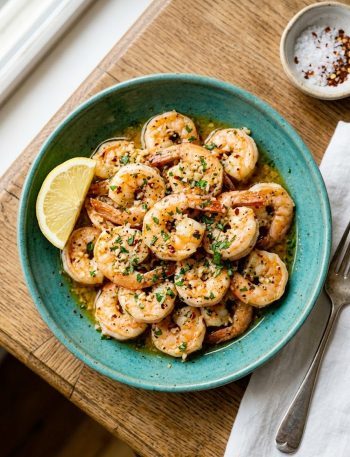Juicy Hawaiian garlic shrimp coated in golden garlic butter sauce garnished with fresh parsley and lemon wedges in a teal ceramic bowl