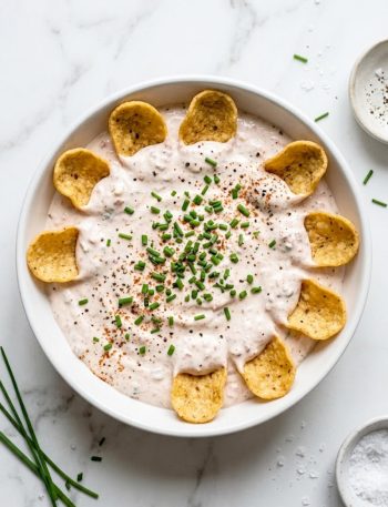 Healthy high-protein pool dip made with Greek yogurt and cottage cheese served in a white bowl with Frito Scoops and fresh chives on top
