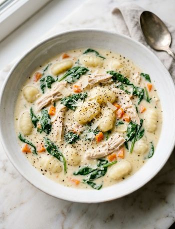 Creamy Olive Garden style chicken gnocchi soup with shredded chicken, pillowy gnocchi, fresh spinach and diced carrots in a white bowl on a marble surface