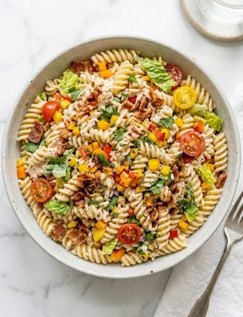 A large serving bowl of simple ranch BLT pasta salad filled with rotini pasta, crispy bacon, halved cherry tomatoes, chopped romaine lettuce, and colorful bell peppers coated in creamy ranch dressing