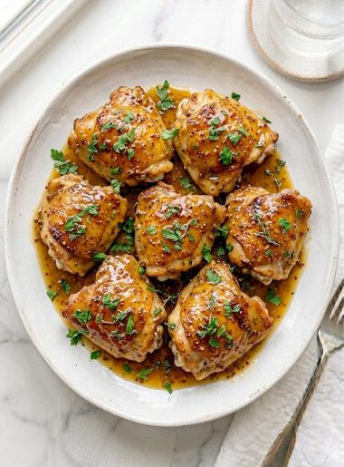 Golden slow cooker honey mustard chicken thighs coated in a rich sweet and tangy honey mustard glaze garnished with fresh parsley on a white serving plate