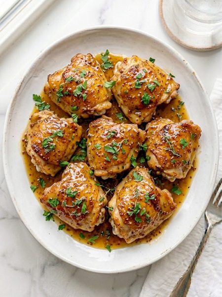 Golden slow cooker honey mustard chicken thighs coated in a rich sweet and tangy honey mustard glaze garnished with fresh parsley on a white serving plate