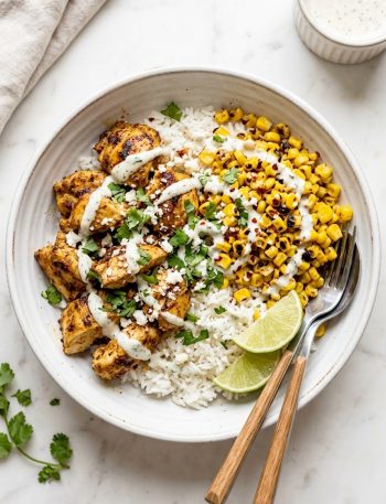 Protein packed street corn chicken bowl with smoky spiced chicken charred corn fluffy rice and creamy cilantro lime drizzle in a white ceramic bowl on a marble surface