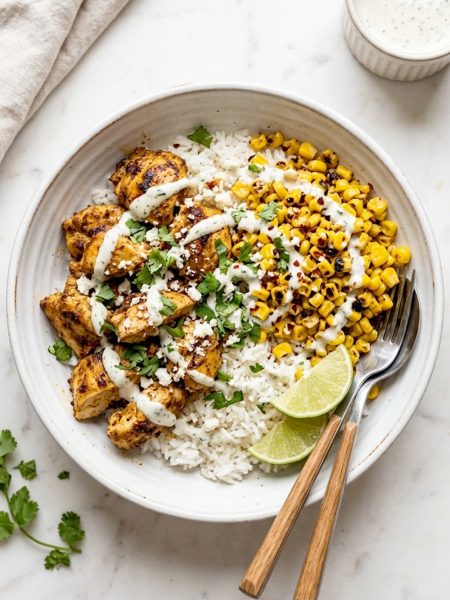 Protein packed street corn chicken bowl with smoky spiced chicken charred corn fluffy rice and creamy cilantro lime drizzle in a white ceramic bowl on a marble surface