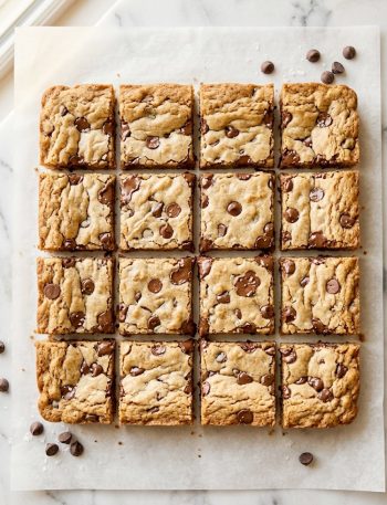 Overhead shot of soft and chewy chocolate chip cookie bars cut into squares on parchment paper showing golden edges and melted chocolate chips throughout
