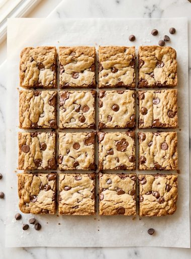 Overhead shot of soft and chewy chocolate chip cookie bars cut into squares on parchment paper showing golden edges and melted chocolate chips throughout
